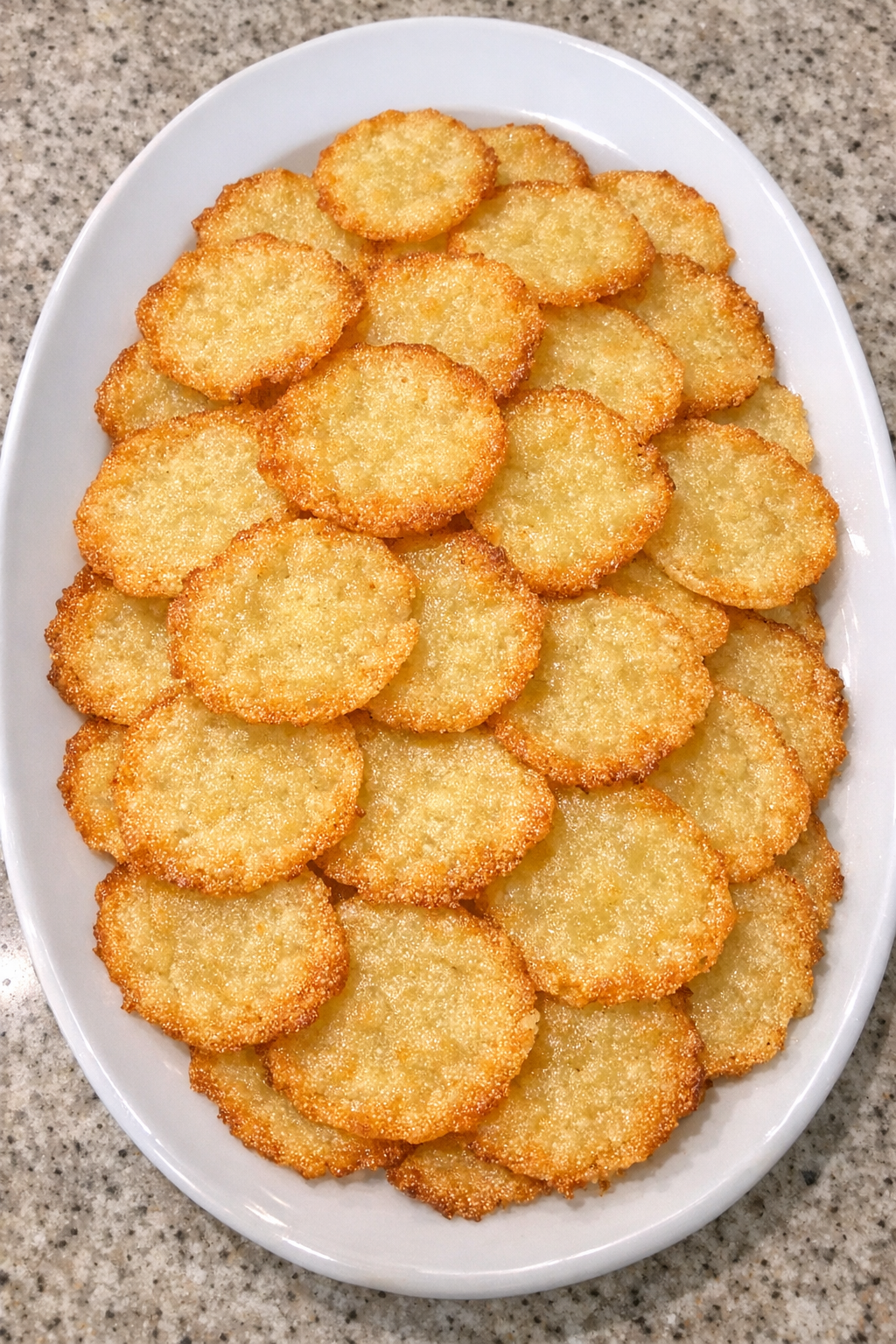 Paper-thin golden buttery potato crackers on a white platter