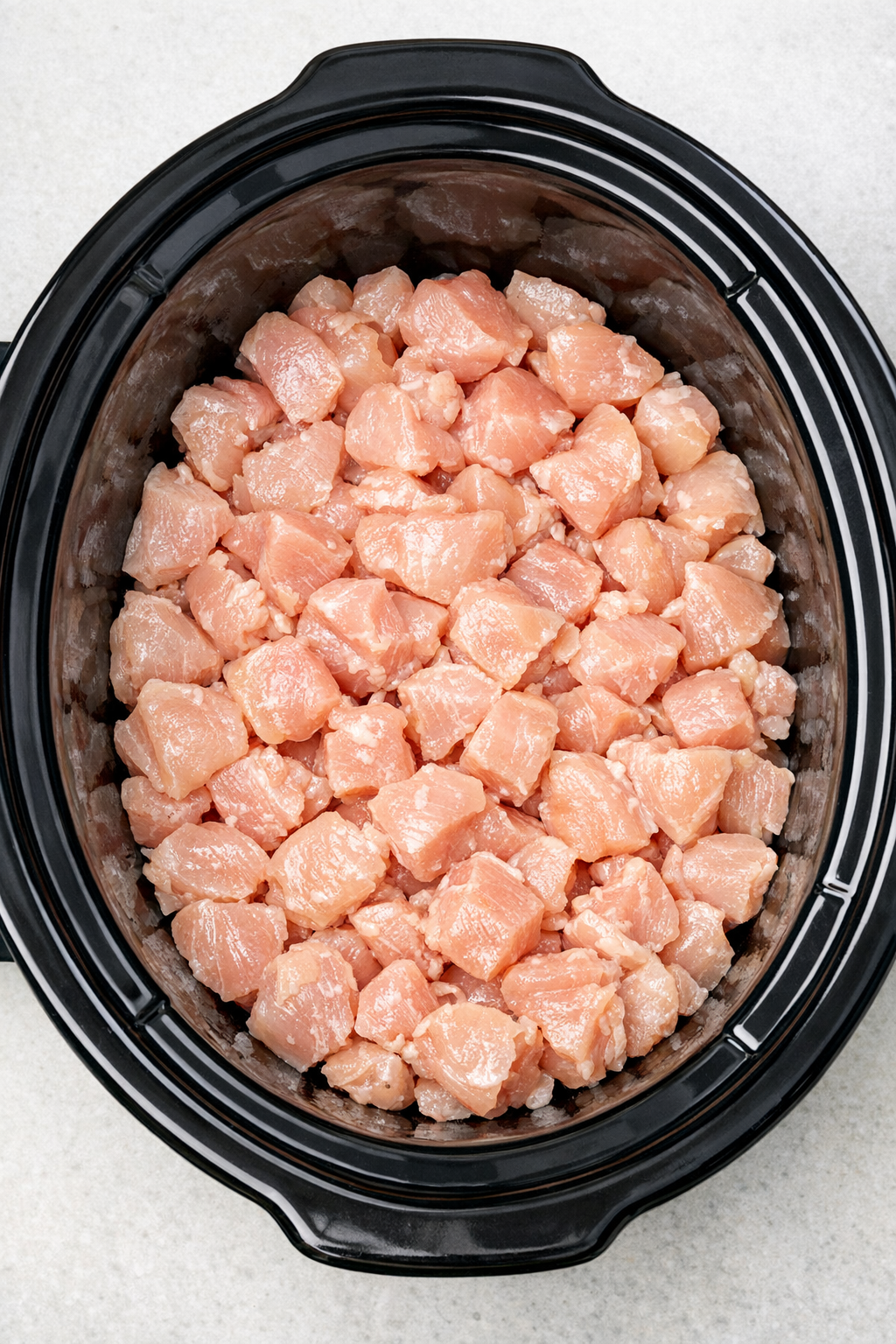 Raw chicken chunks spread in the slow cooker
