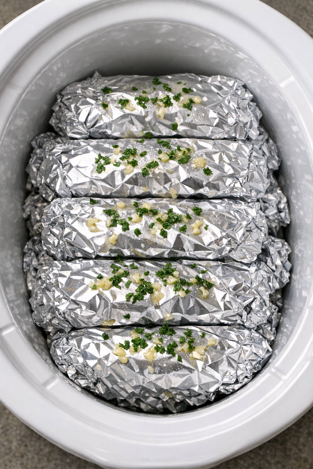 Slow cooker foil packets stacked inside a white slow cooker