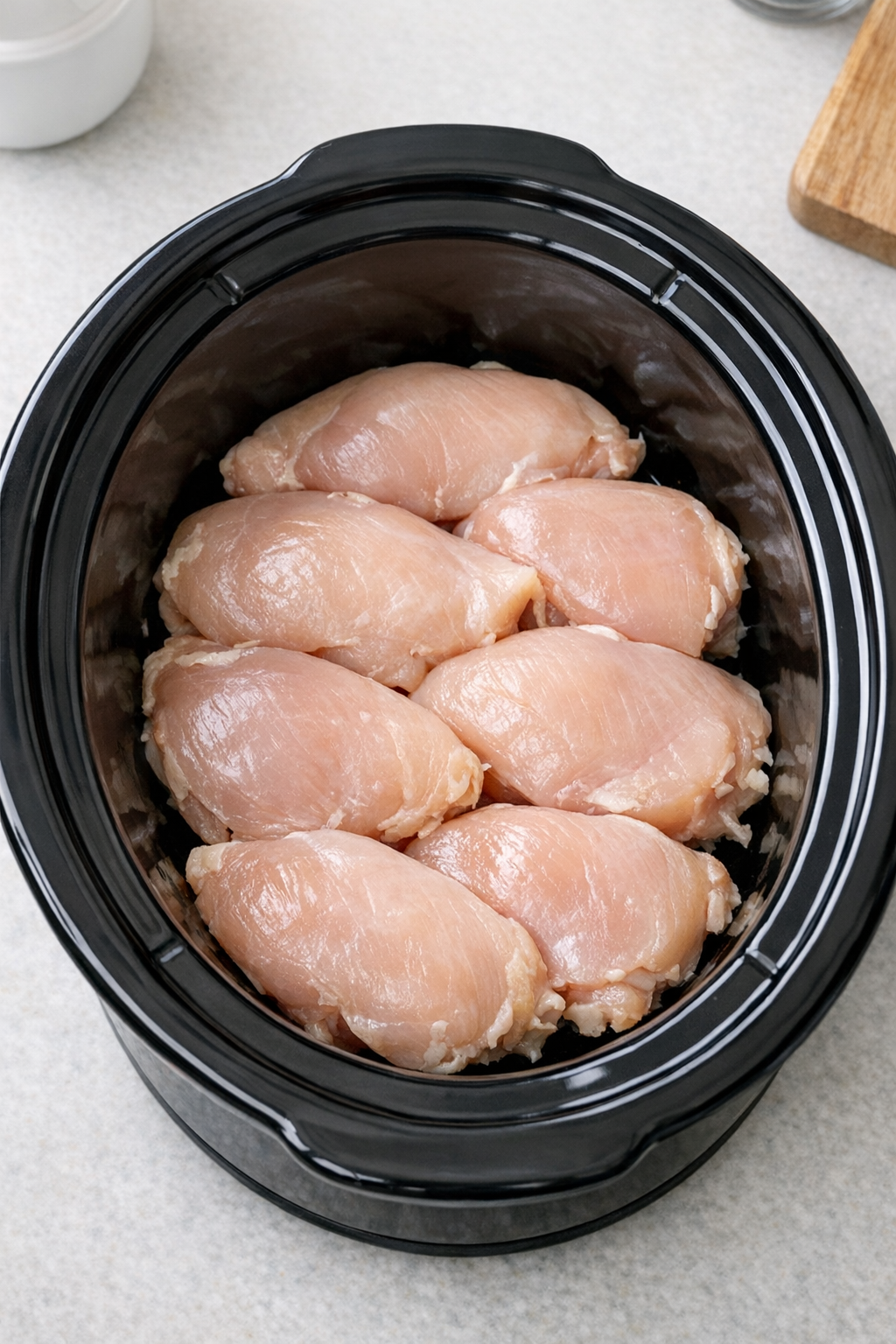 Raw chicken breasts arranged in black slow cooker