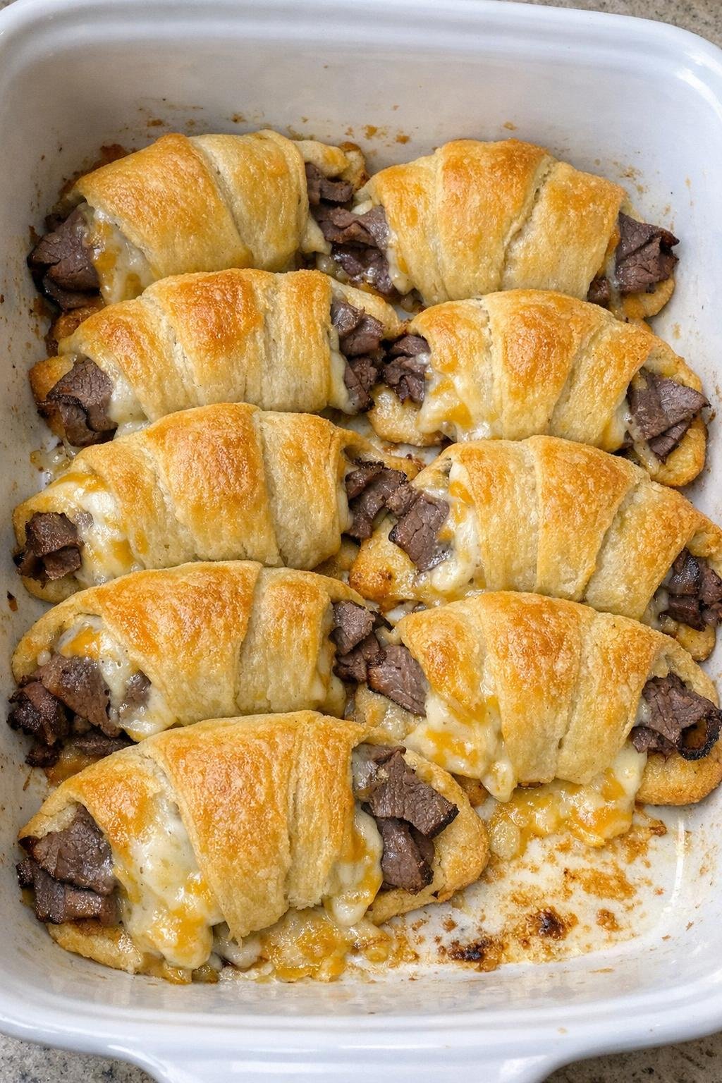 Flaky golden crescent rolls stuffed with roast beef and melted colby jack cheese in a white casserole dish
