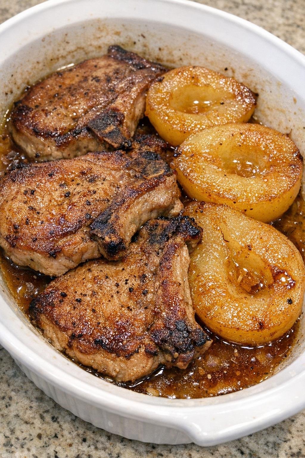 Golden browned pork chops with caramelized pear halves in a white oval casserole dish