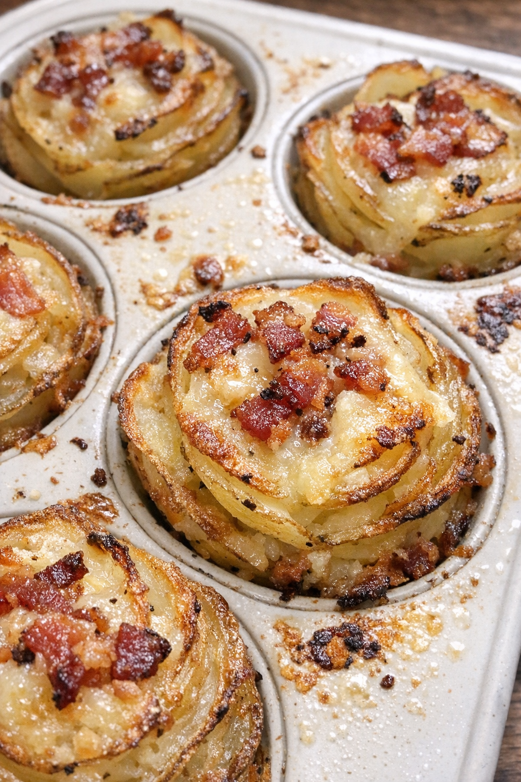 Golden layered potato blossoms with melted gruyere and crispy bacon bits in a ceramic muffin tin