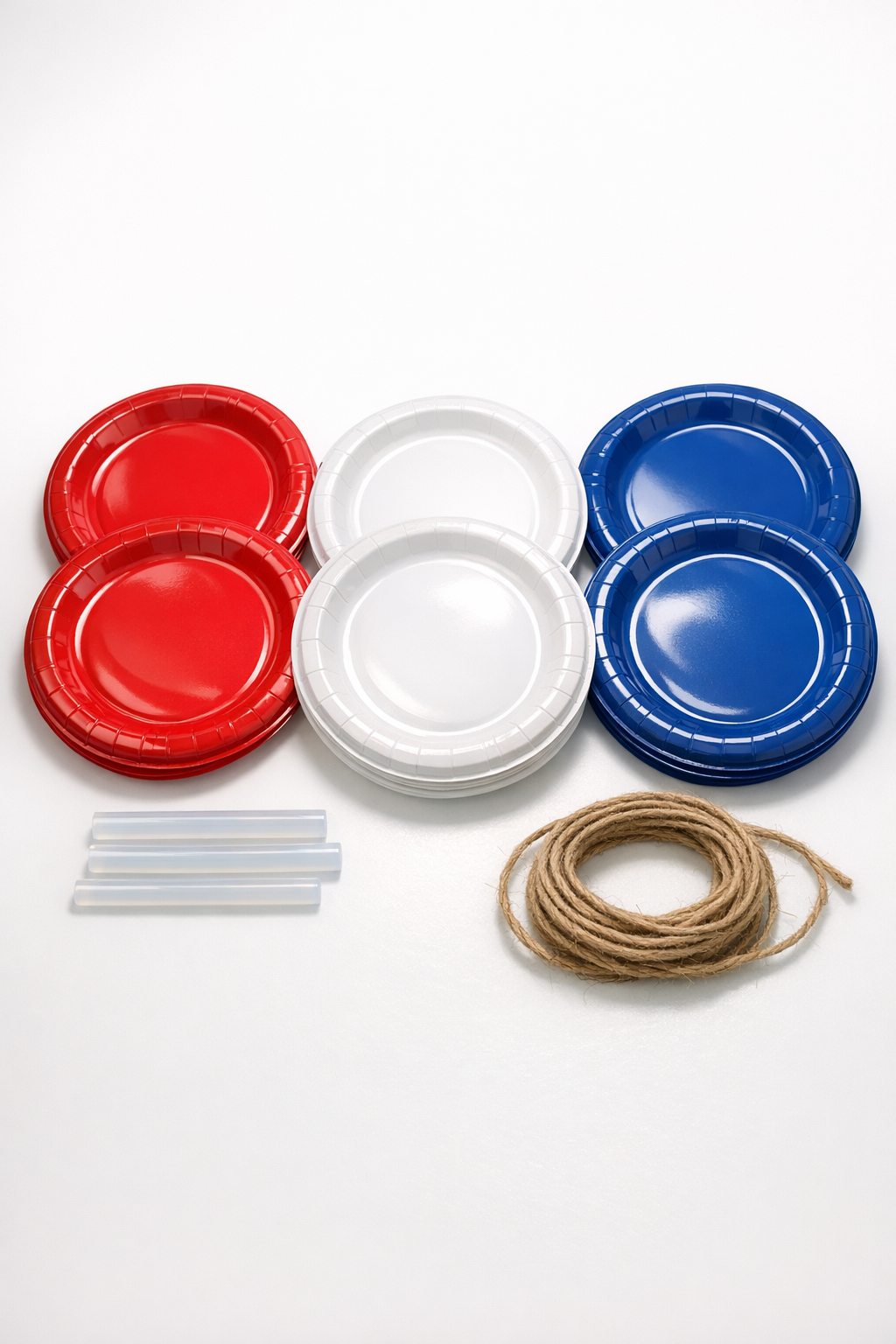 Red, white, and blue plastic plates, hot glue sticks, and twine laid out for the project