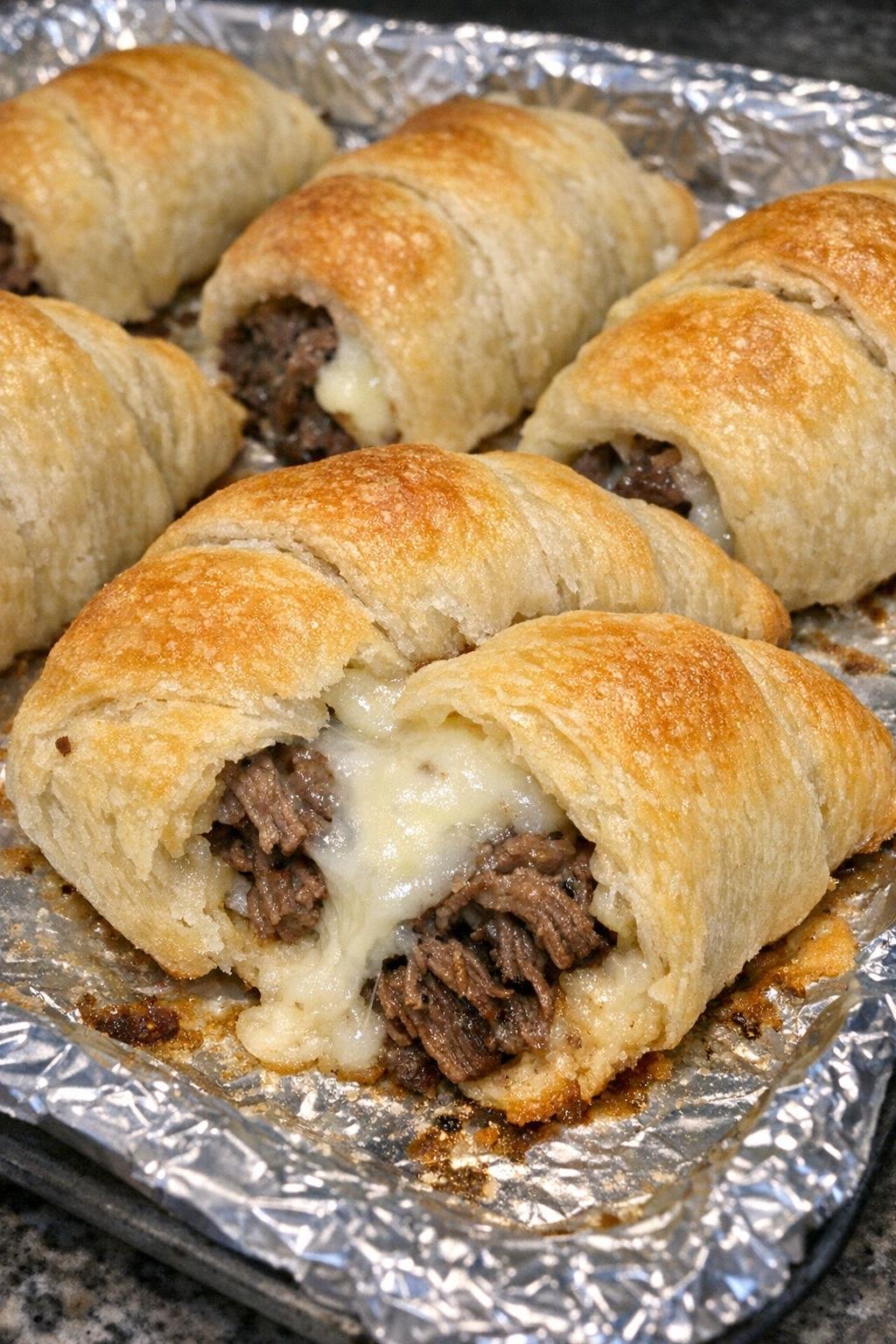 Oven baked beef and swiss bundles on a foil-lined baking sheet
