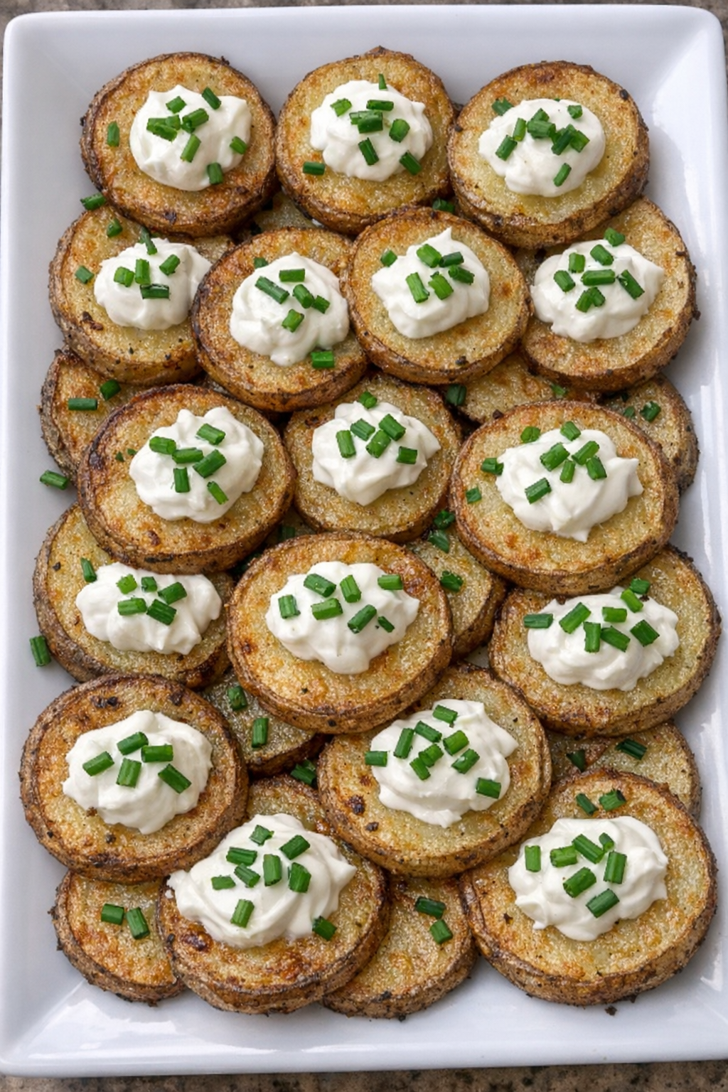 Golden crispy potato rounds topped with sour cream and chives on a white platter