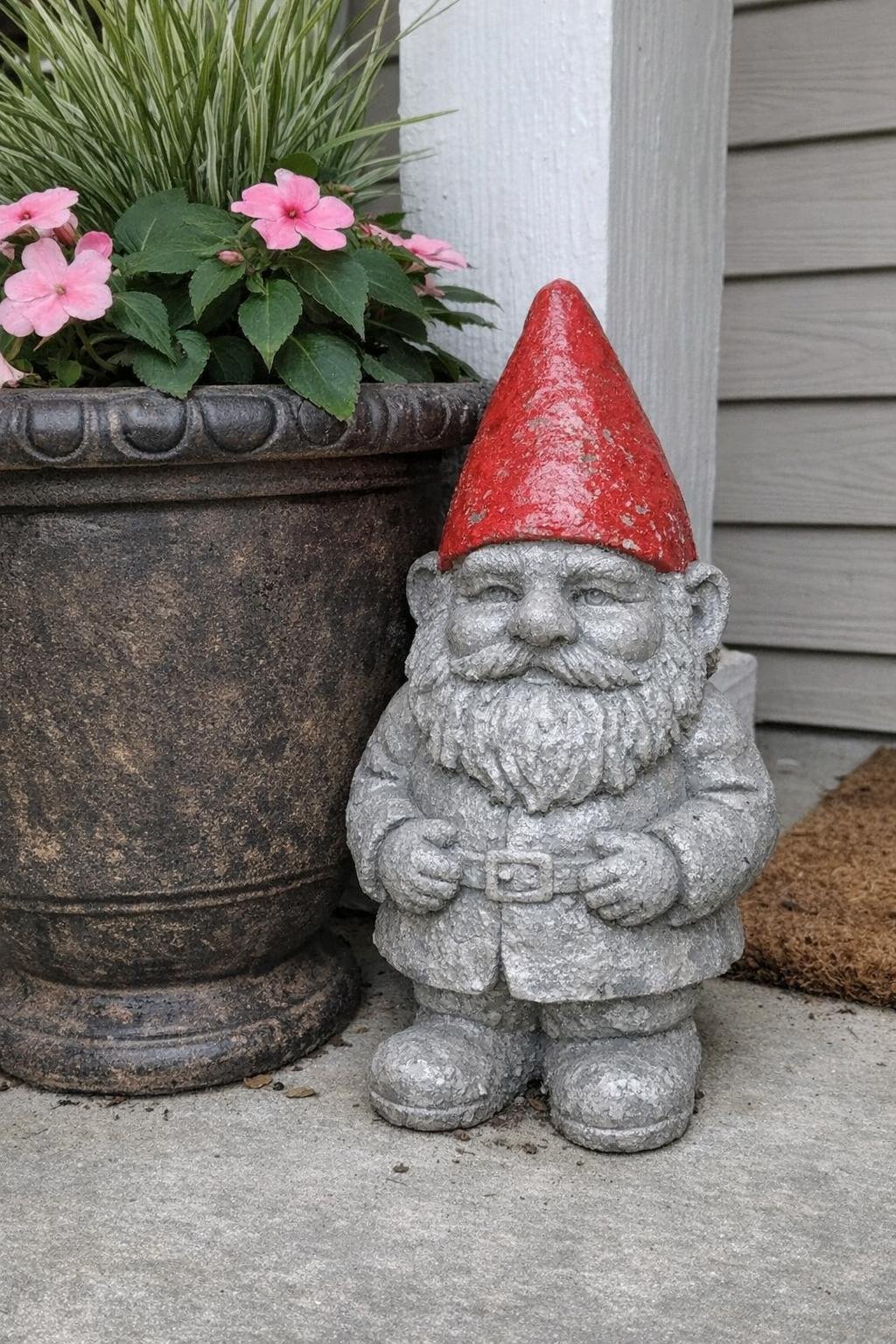 Concrete gnome with a red hat beside a porch pot