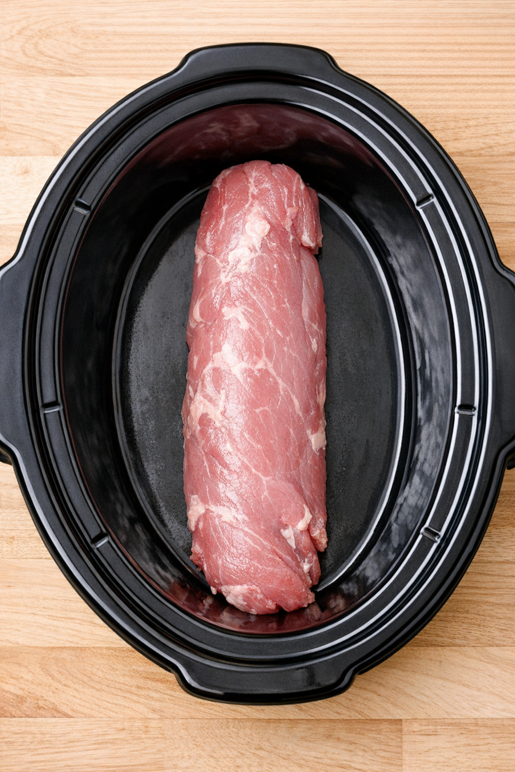 Raw pork tenderloin resting in the bottom of a slow cooker