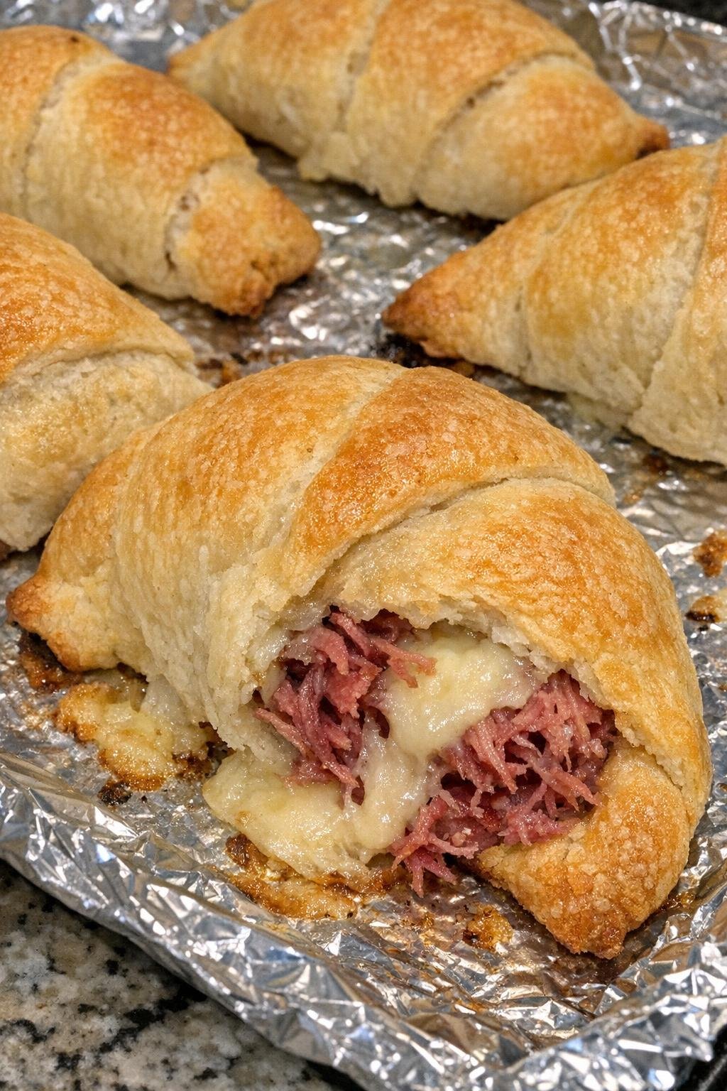 Flaky golden crescent bundles with corned beef and Swiss cheese on a foil-lined baking sheet