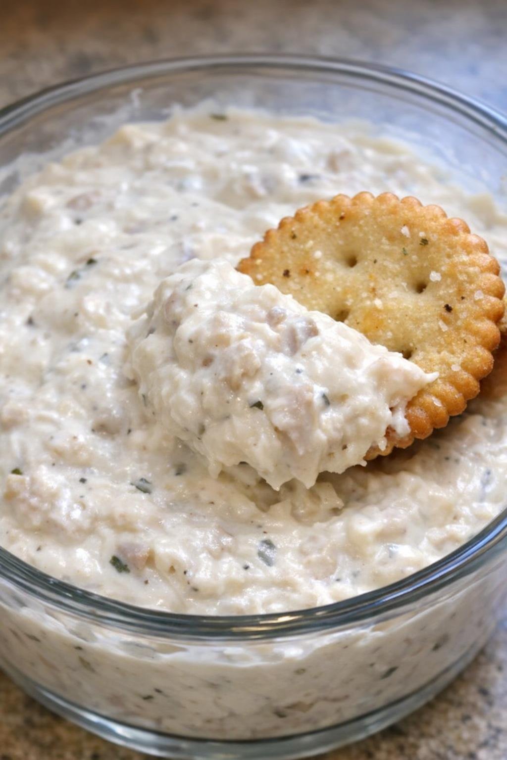 Clam Winslow dip in a glass bowl with a cracker scooping through it
