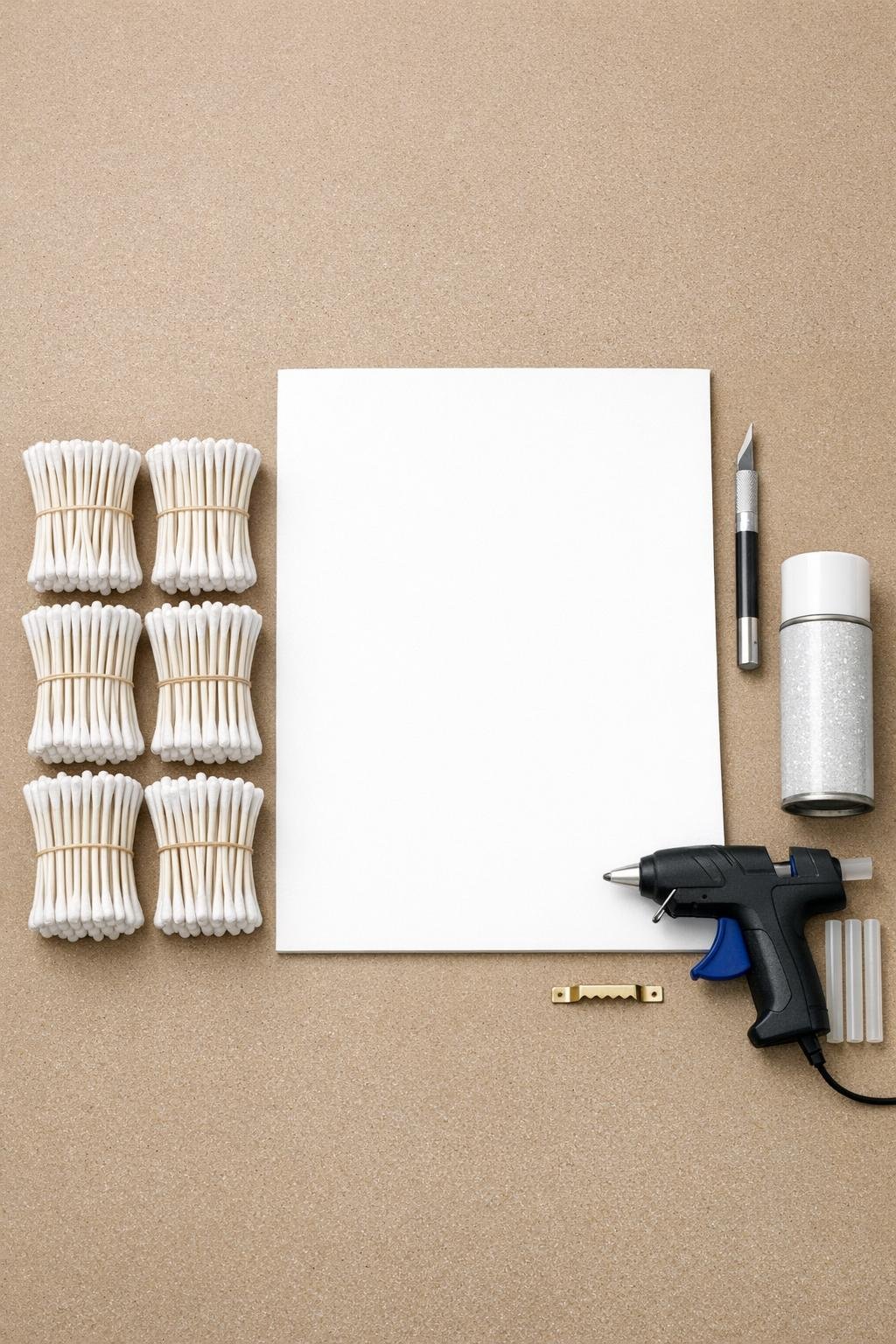 Cotton swabs, foam board, craft knife, hot glue gun, glitter spray, and picture hanger laid out on a craft table