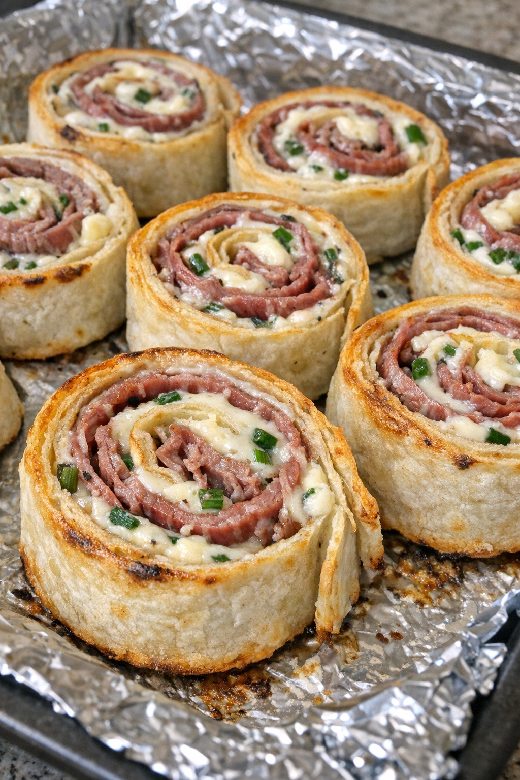Oven baked beef cream cheese pinwheels on a foil-lined baking sheet