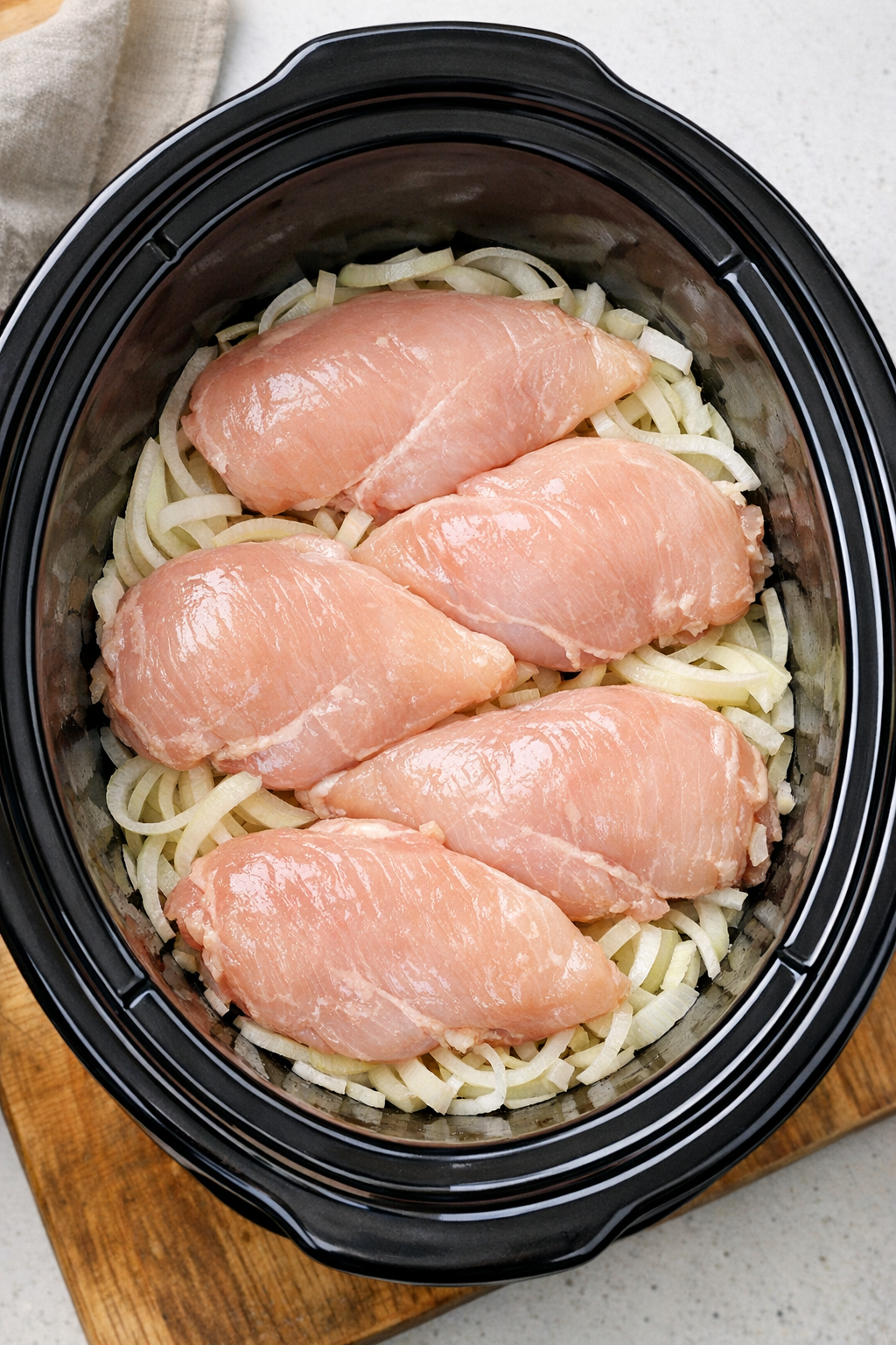 Raw chicken placed over onions in slow cooker