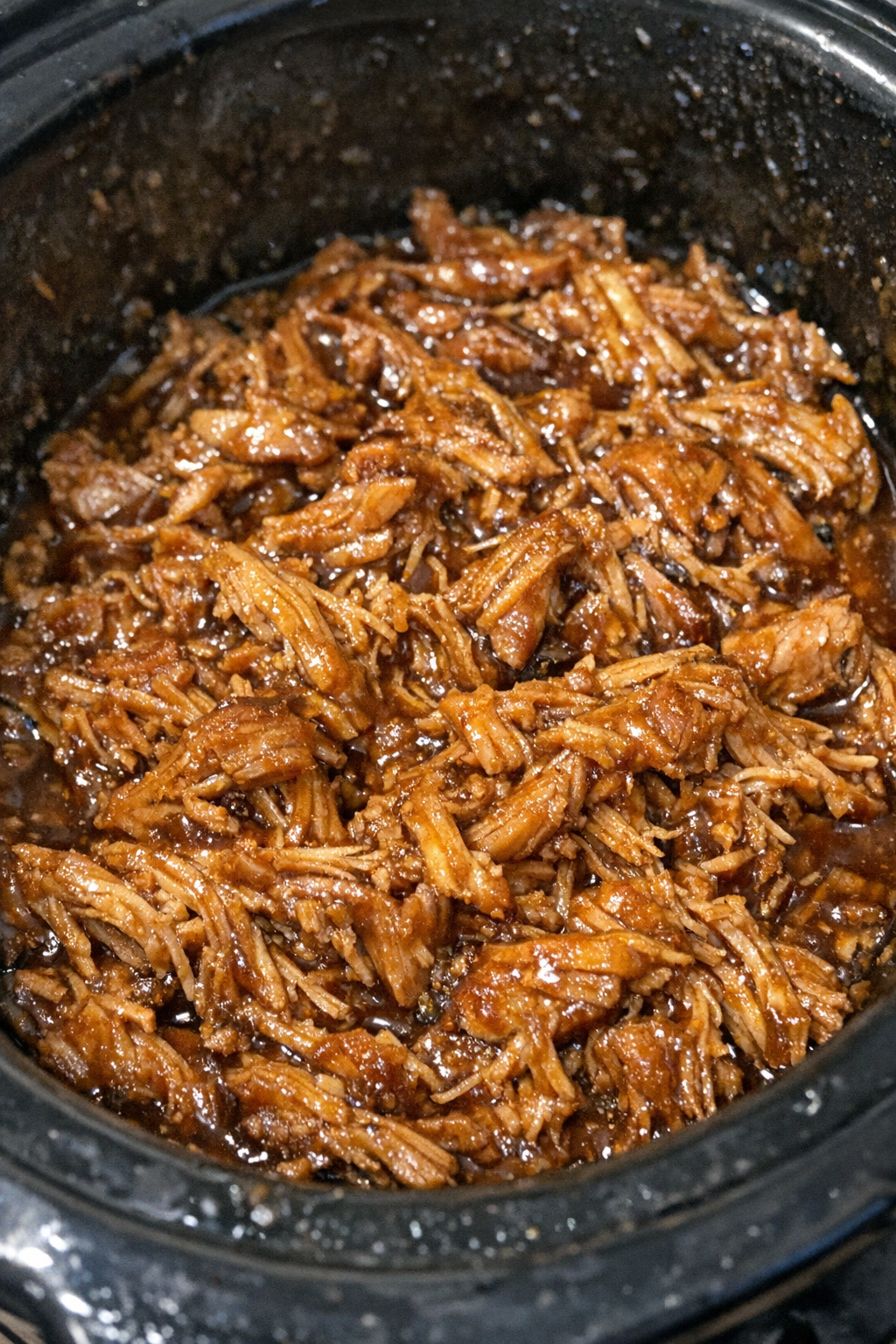 Shredded pork in glossy amber sauce in a slow cooker
