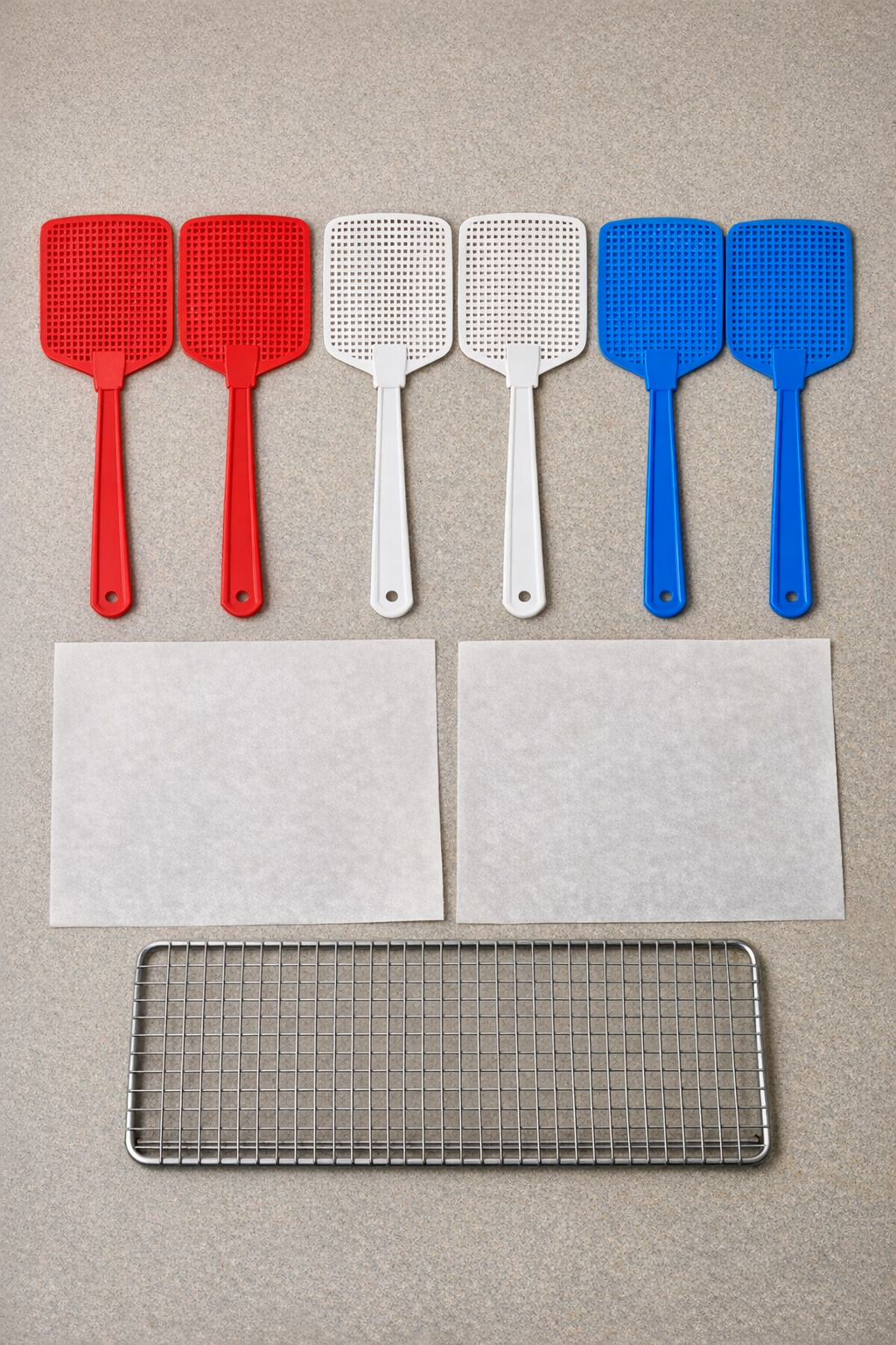 Red, white, and blue fly swatters with parchment paper and a wire cooling rack laid out neatly