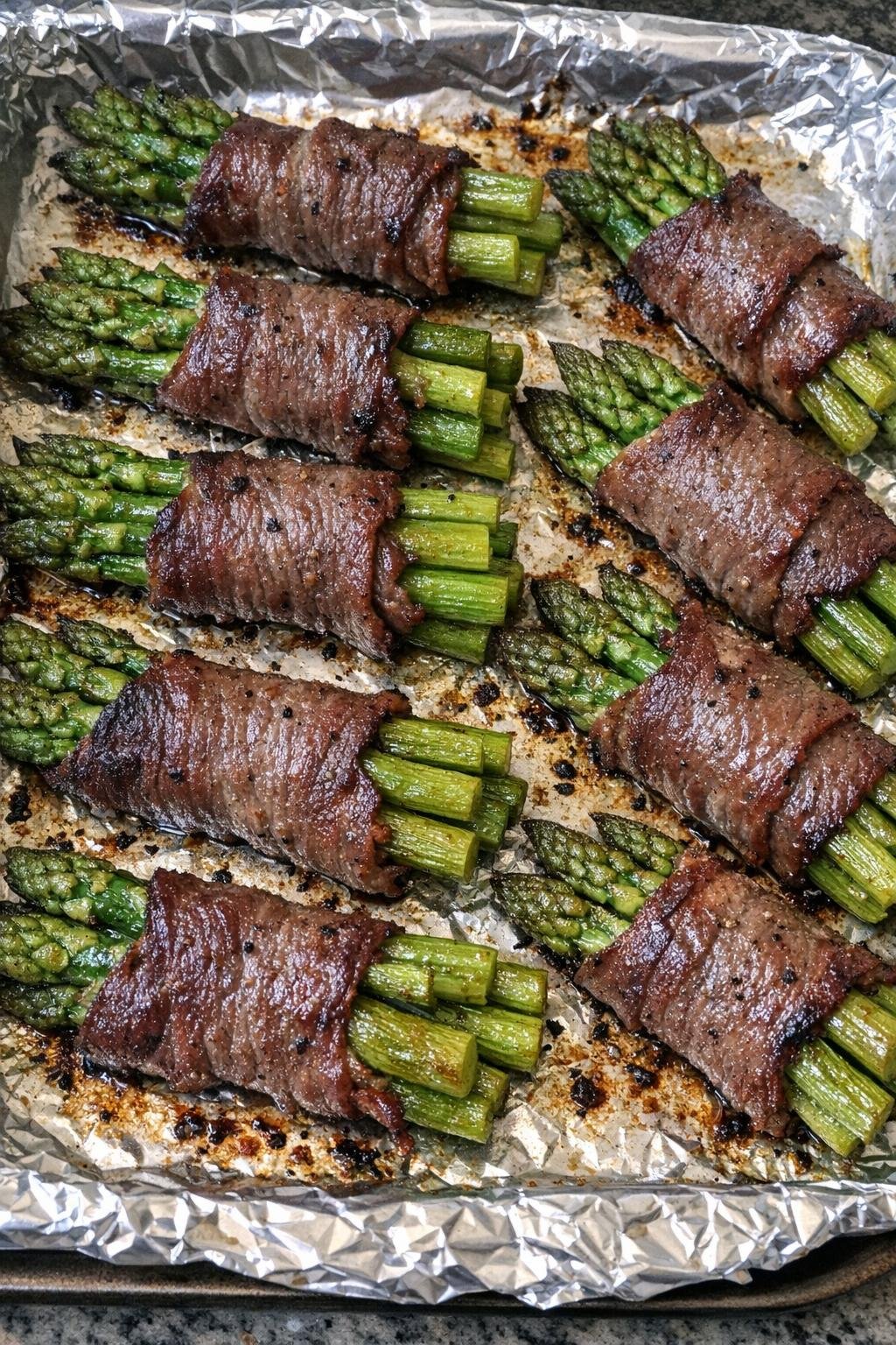 Oven baked beef wrapped asparagus on a foil-lined baking sheet