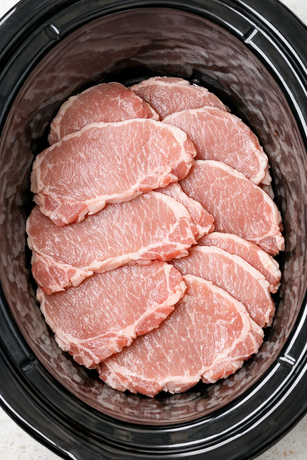 Raw thin-cut pork chops arranged in slow cooker