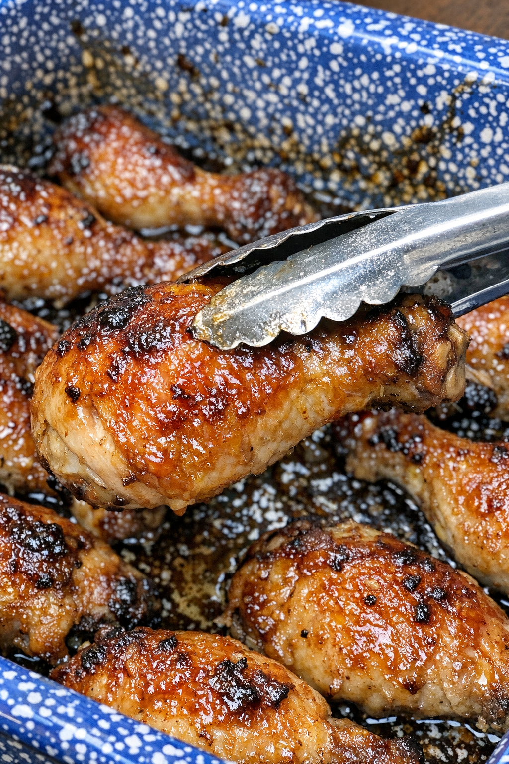 Golden glazed chicken drumsticks and thighs in a blue speckled enamel baking dish