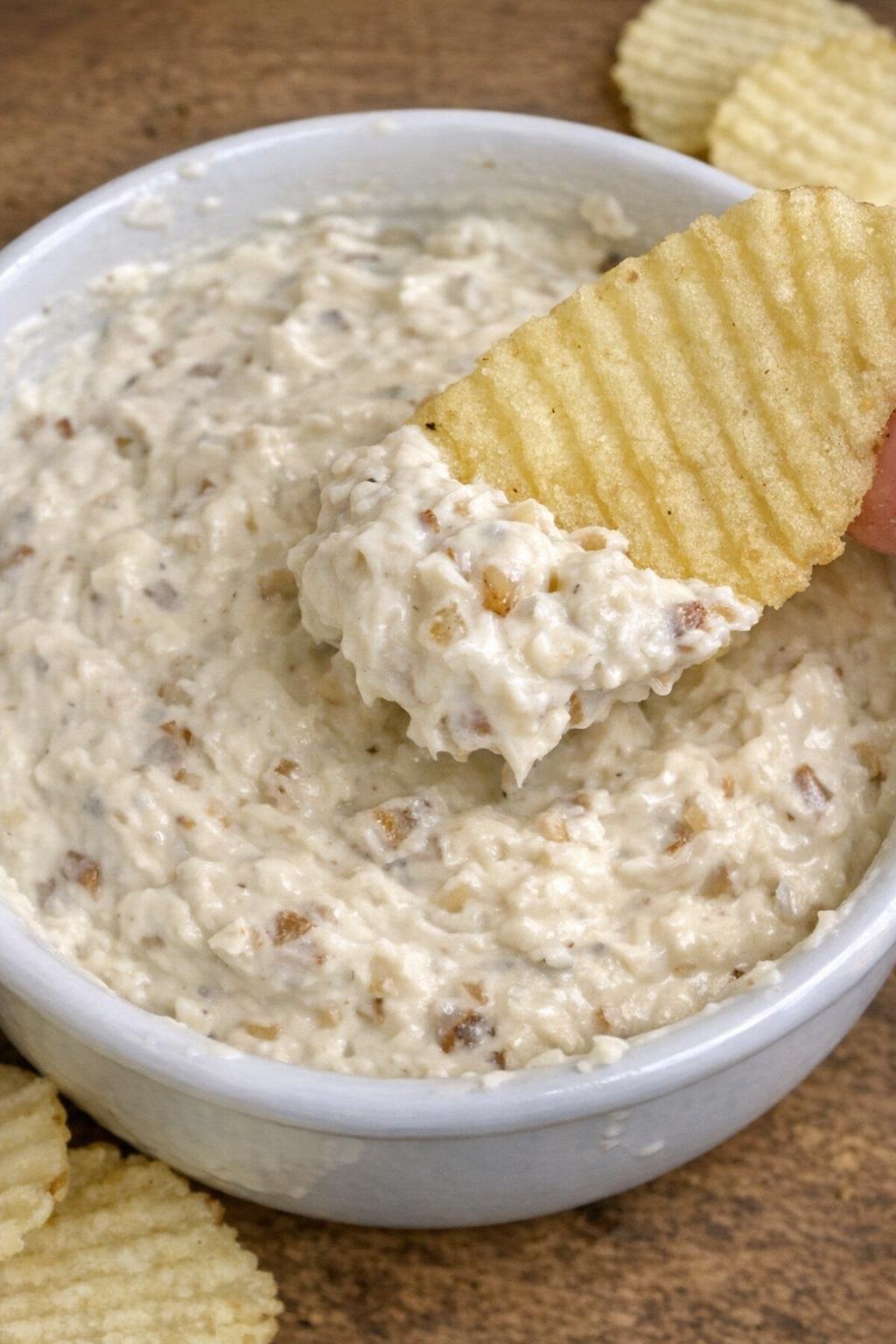 3-ingredient onion hawthorne dip in a white bowl with a potato chip scooping dip