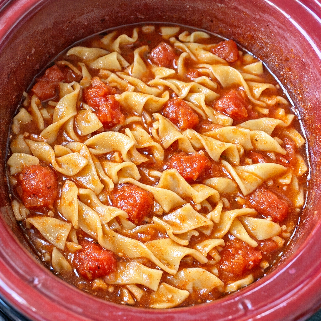 Slow cooker Amish tomato noodle soup in a red slow cooker