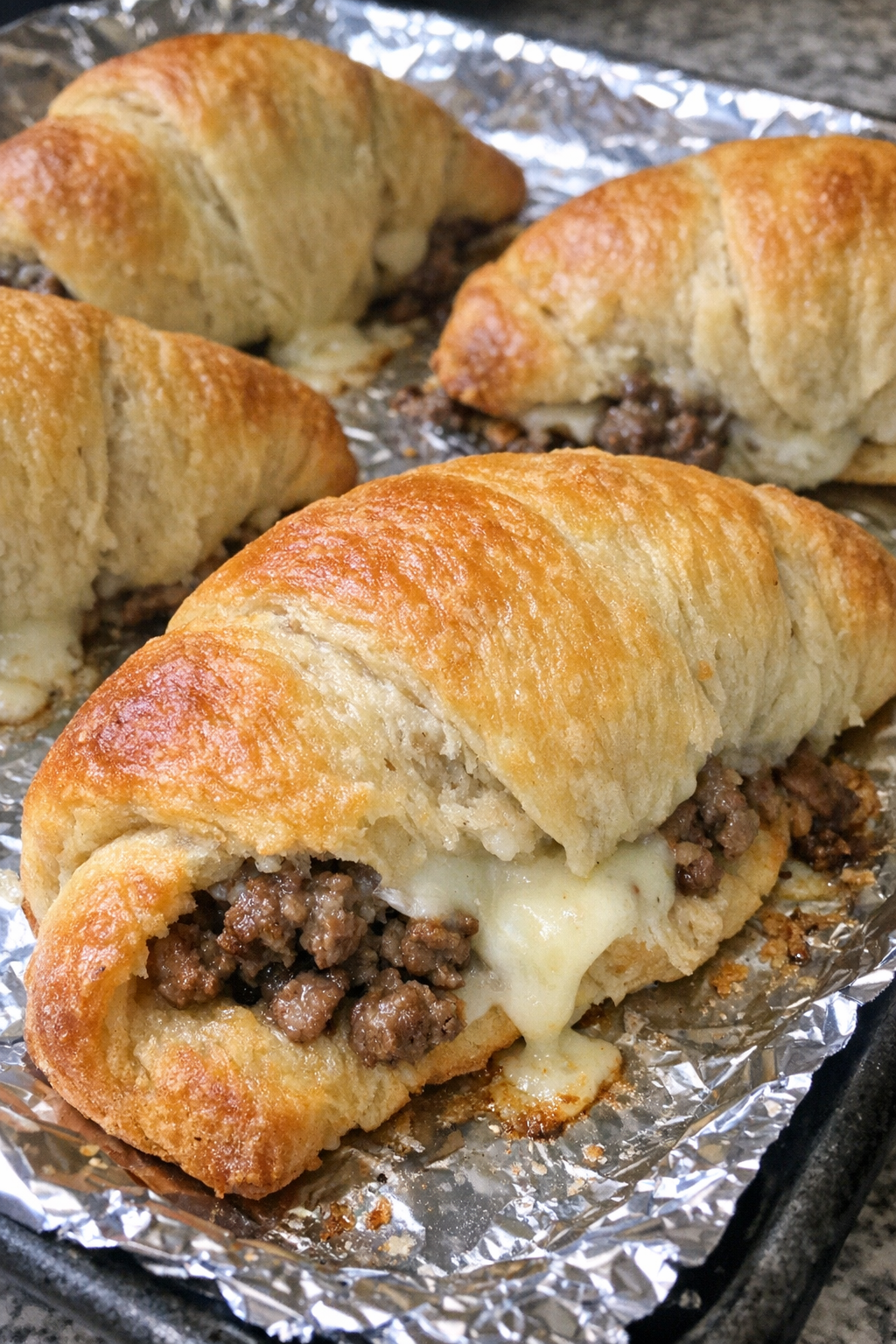 Oven baked beef crescent sandwiches on a foil-lined baking sheet