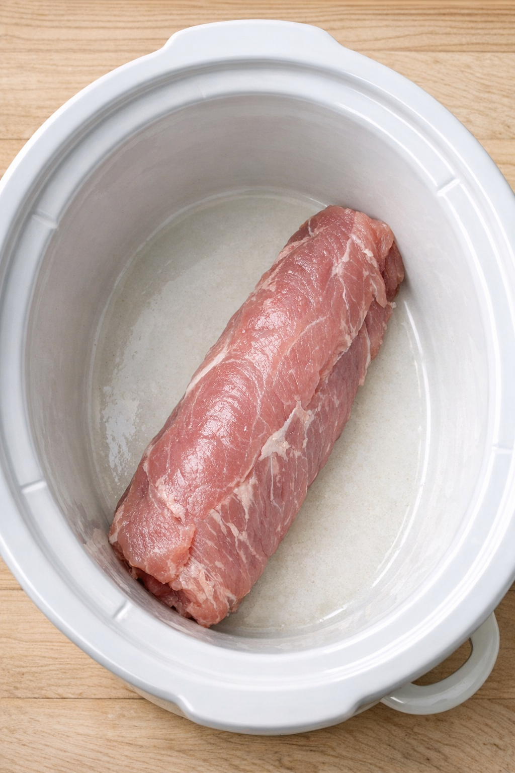 Raw pork tenderloin placed in a slow cooker