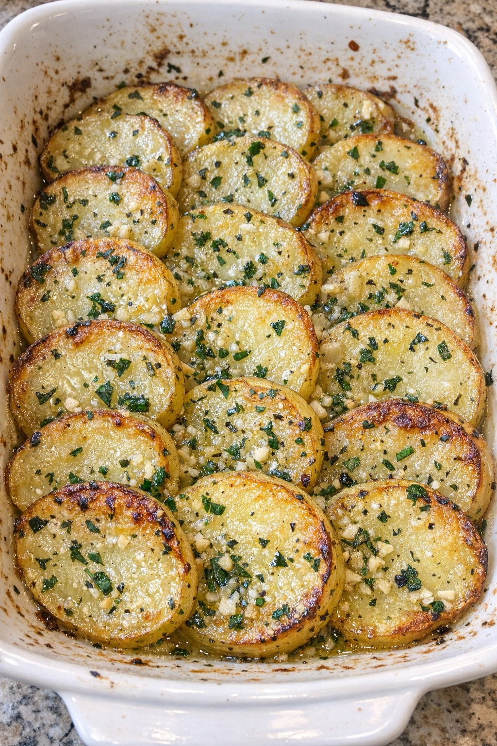 Tender sliced potatoes with herb butter glaze and golden edges in a white casserole dish