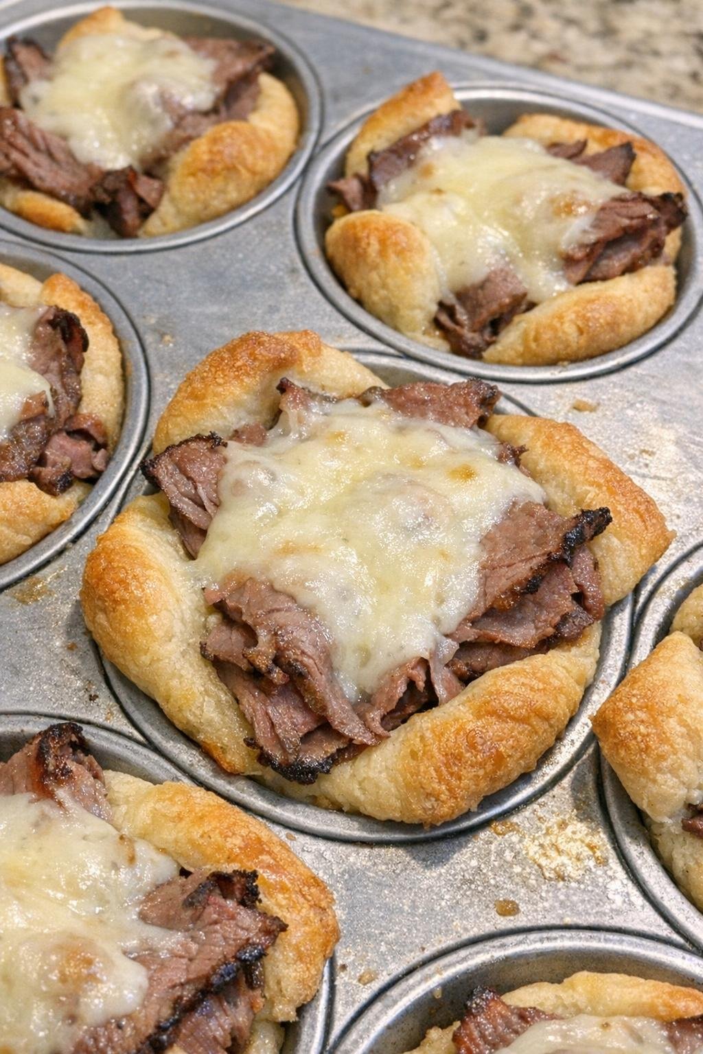Golden brown crescent dough cups filled with roast beef and melted fontina in a muffin tin