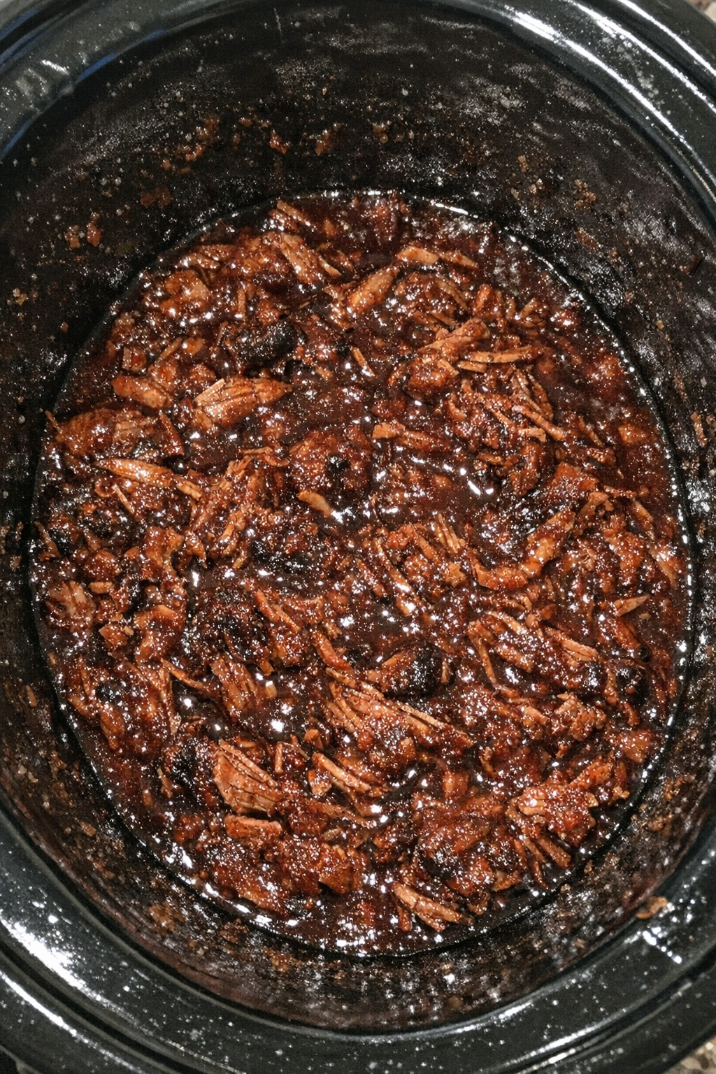 Slow cooker filled with shredded meat in a dark crimson glaze