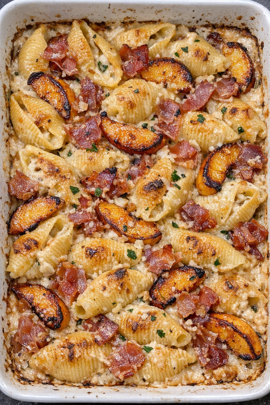 Golden baked pasta shells with roasted peaches, prosciutto, and creamy sauce in a baking dish
