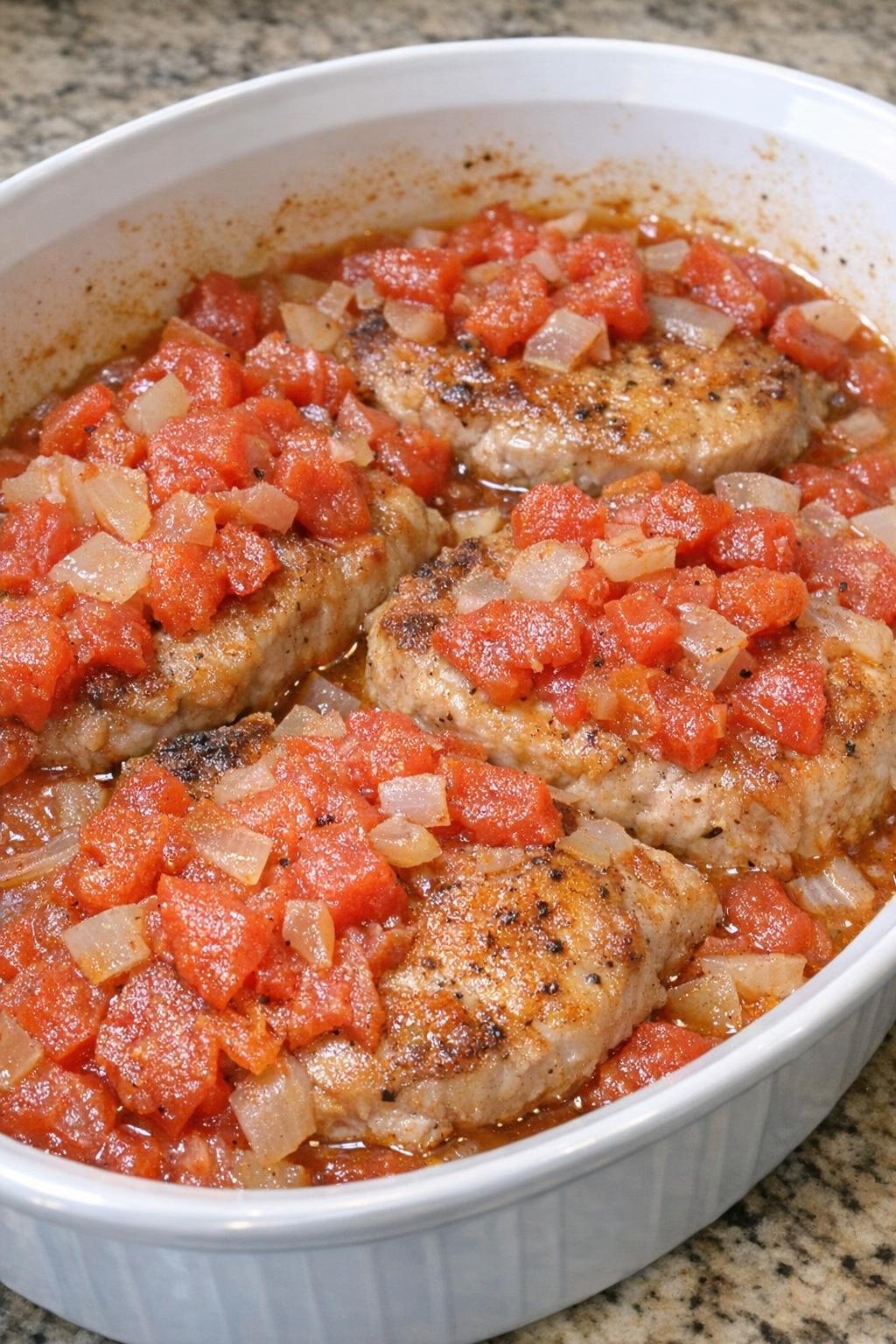 Tender pork chops baked with diced tomatoes and onion in a white casserole dish
