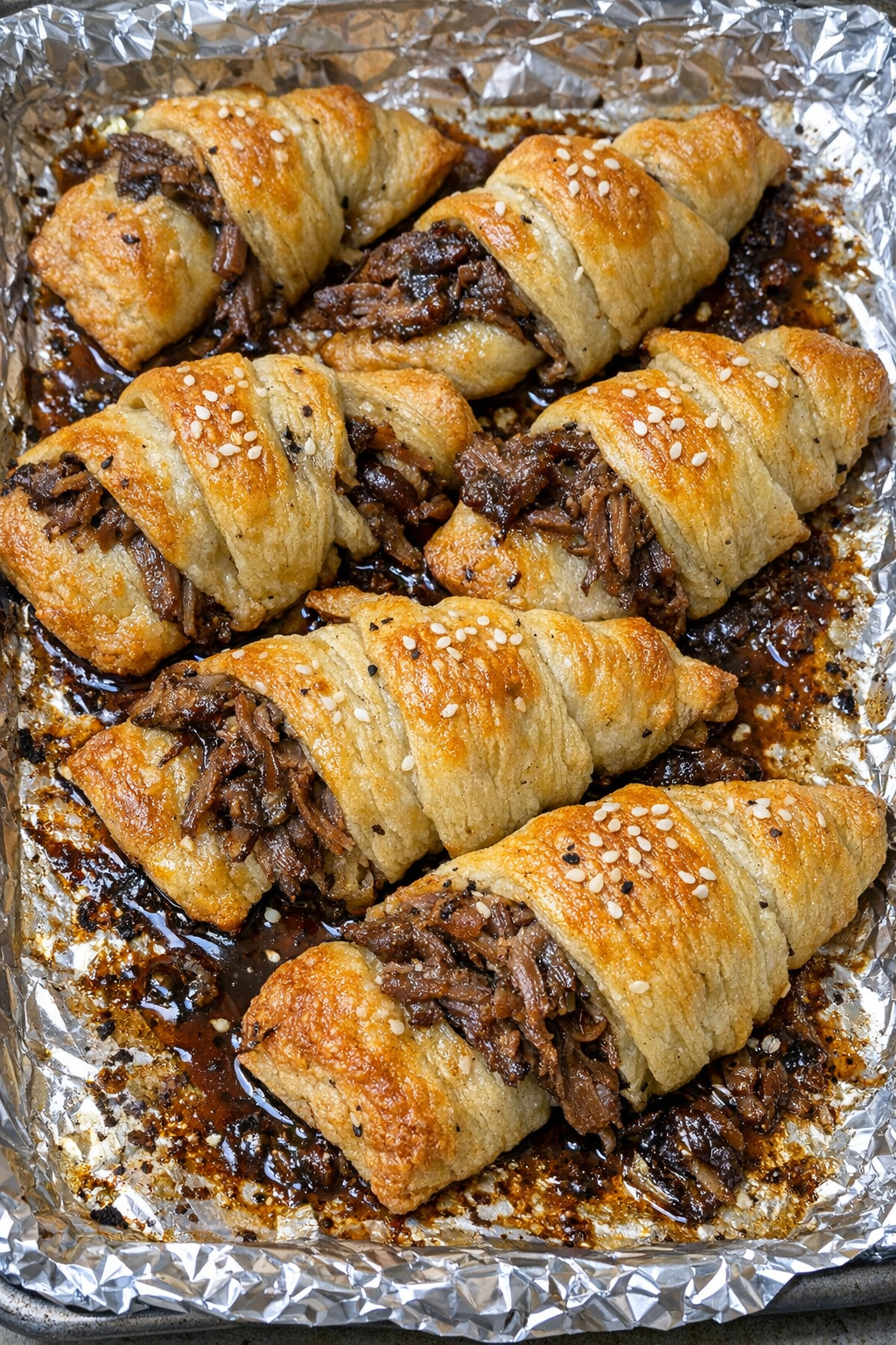 Oven baked beef crescent knots on a foil-lined baking sheet