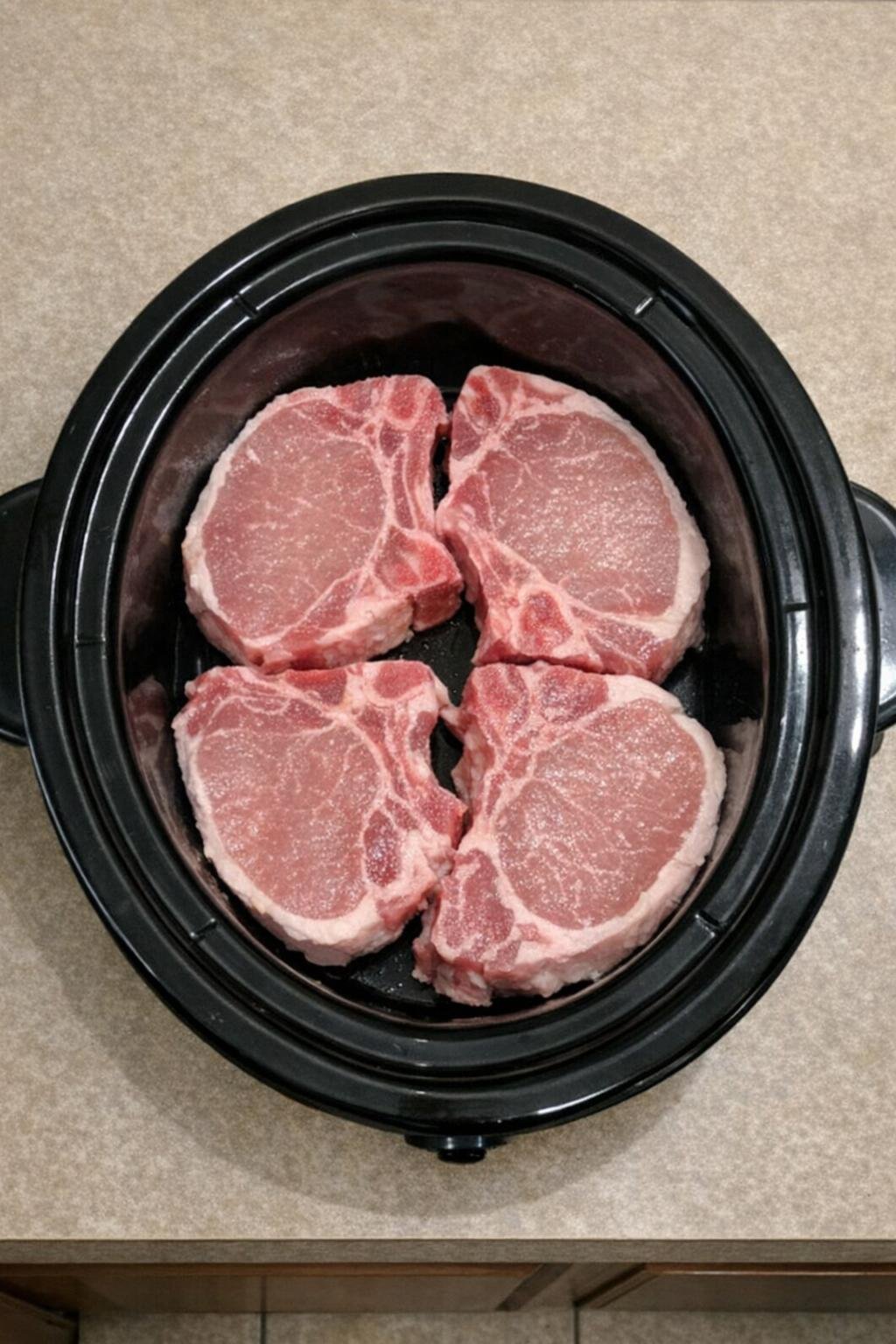 Raw pork chops arranged in the slow cooker