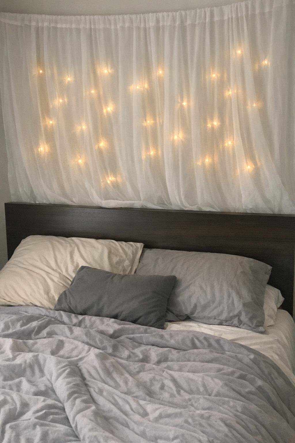 String lights glowing behind a sheer white curtain above a bed