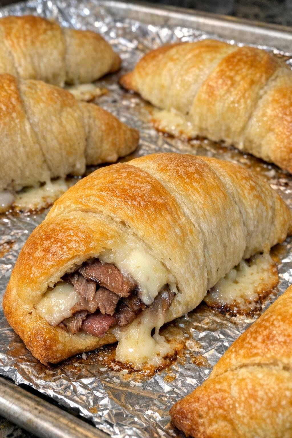 Golden brown crescent dough pockets filled with roast beef and taleggio cheese on a foil-lined baking sheet
