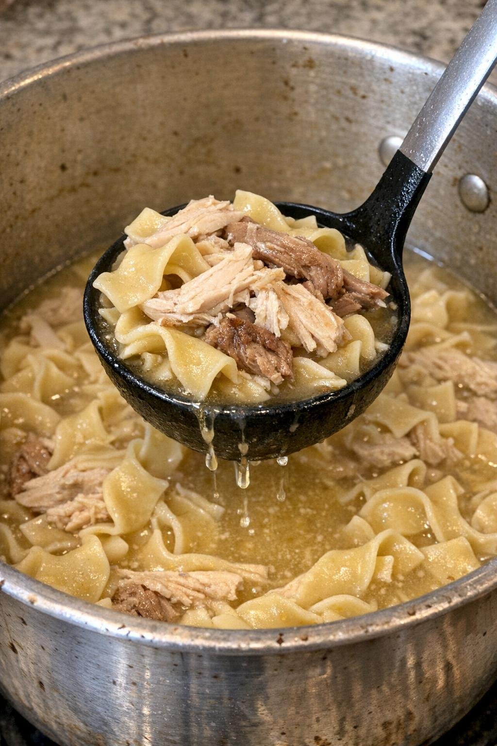 Turkey noodle soup in a dented pot with a ladle lifting noodles and turkey