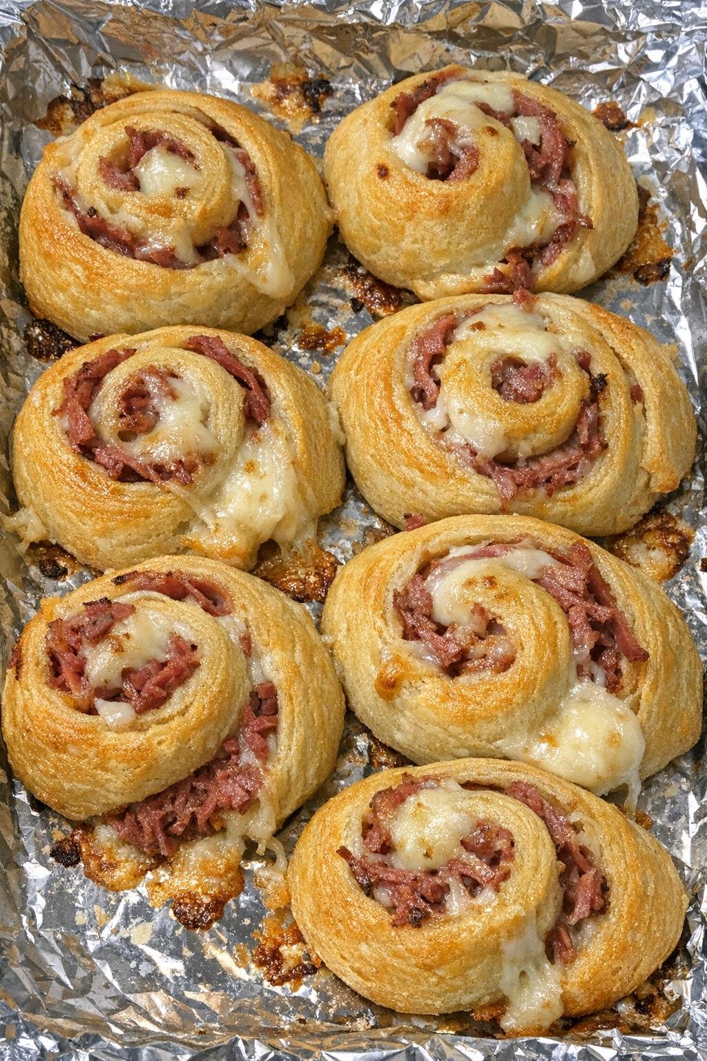 Spiral-shaped golden crescent wheels with corned beef and melted provolone on a foil-lined baking sheet