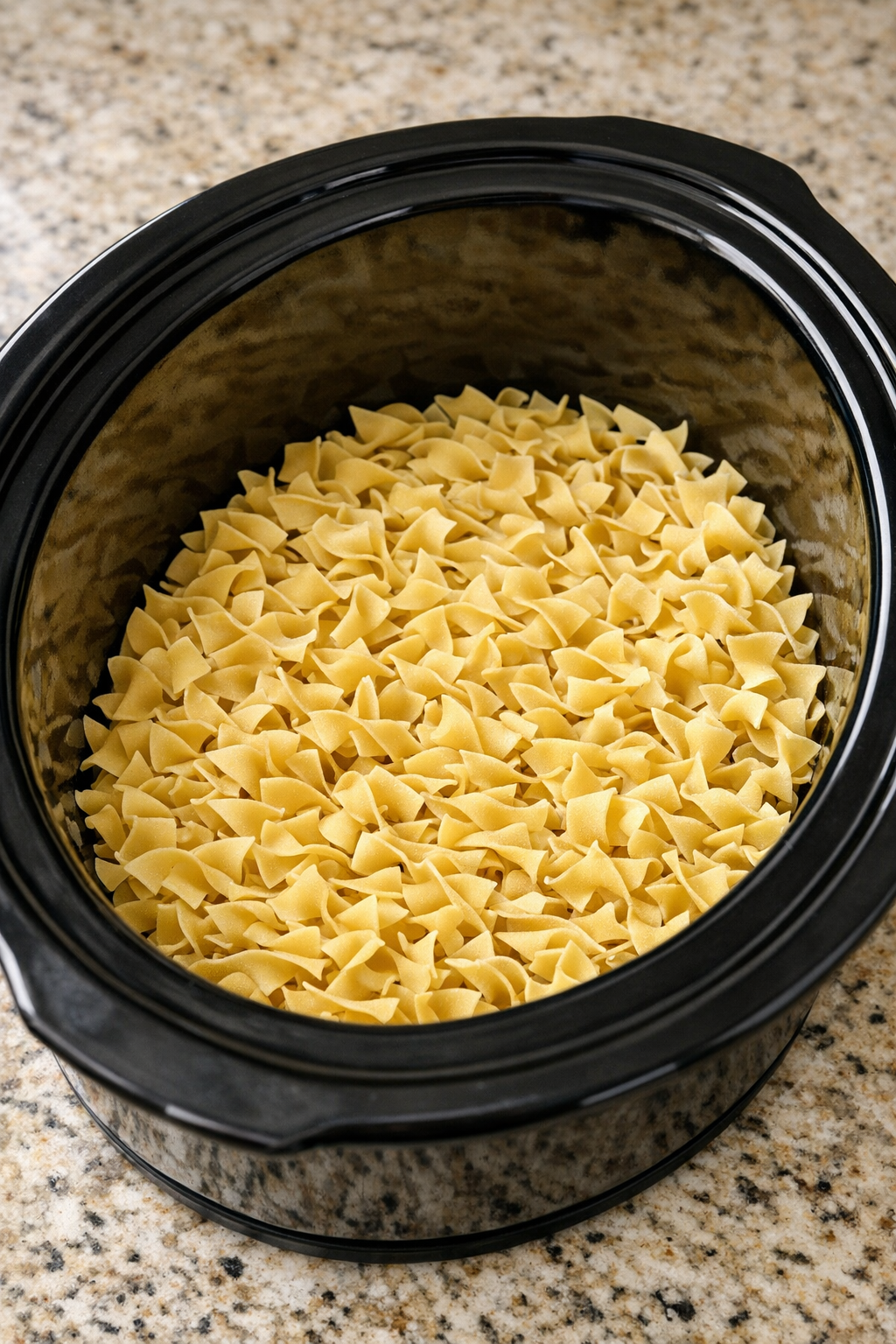 Dry egg noodles spread across the bottom of a slow cooker