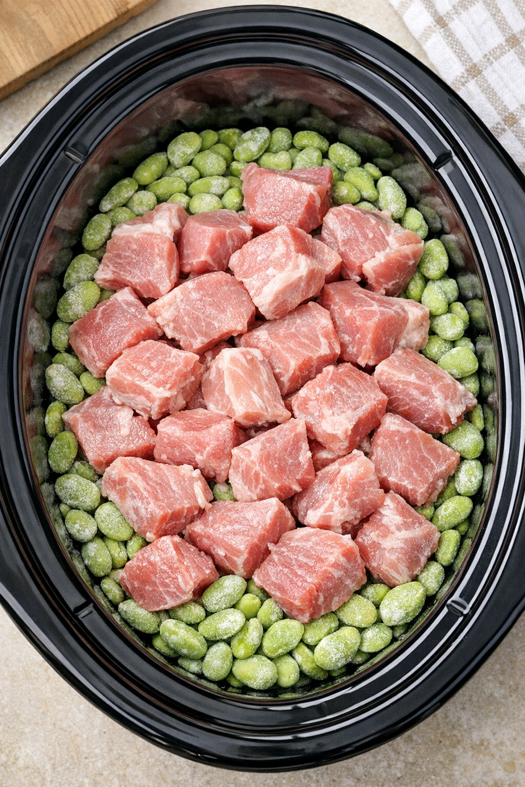 Pork pieces layered over frozen lima beans in a slow cooker