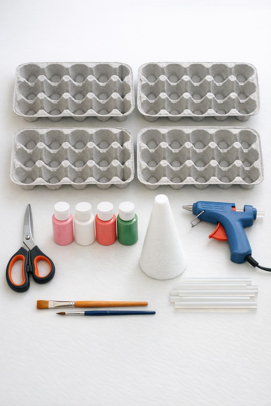 Egg cartons, scissors, paint, foam cone, and glue gun laid out for the project