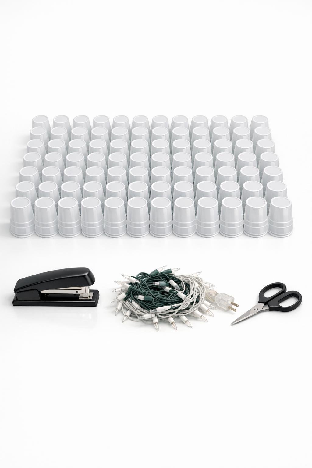 White plastic cups, stapler, mini lights, and scissors laid out for the project