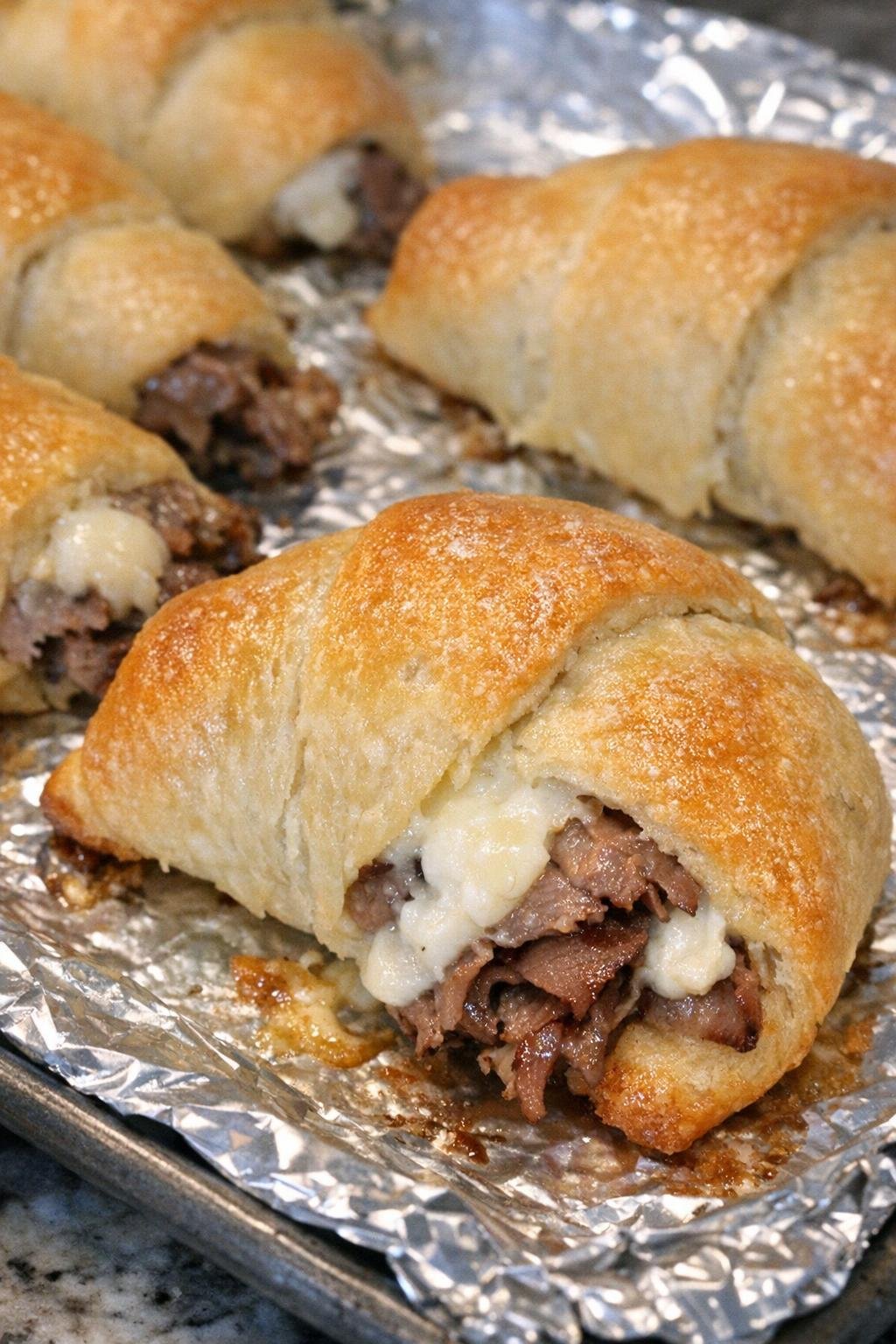 Golden brown crescent dough puffs filled with roast beef and cream cheese on a foil-lined baking sheet