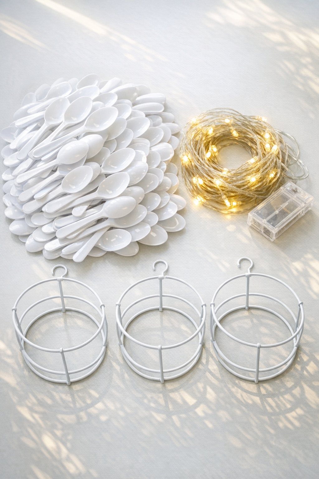 White plastic spoons, clear string lights, and a round wire frame laid out for lantern making