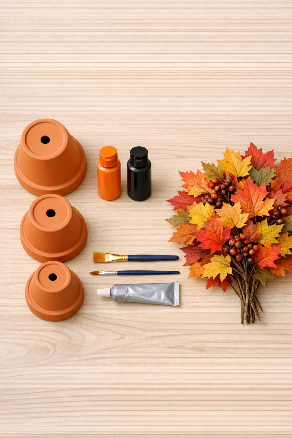 Clay pots, paint, glue, and faux leaves laid out for the project