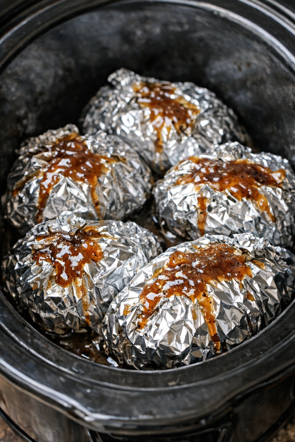 Slow cooker beef and bacon foil packets in a black slow cooker