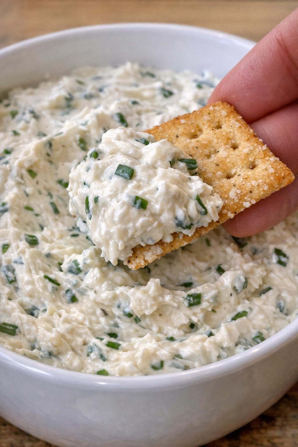 Chive Preston dip in a white bowl with a cracker scooping it