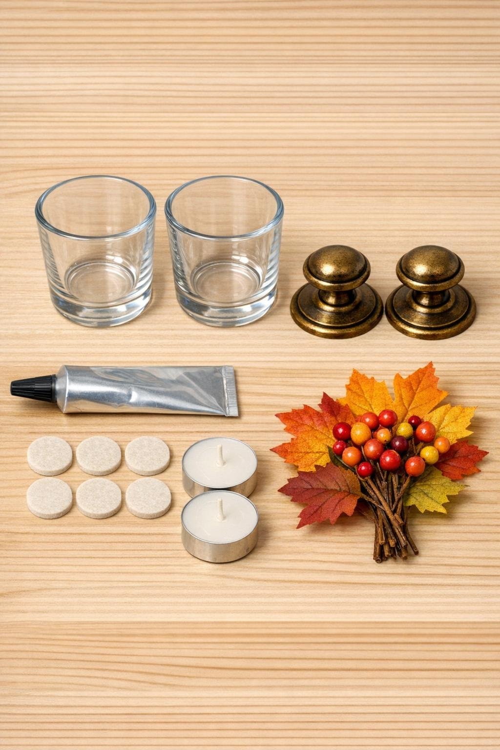 Glass votive cups, brass drawer pulls, adhesive, felt pads, and faux fall accents laid out on a table