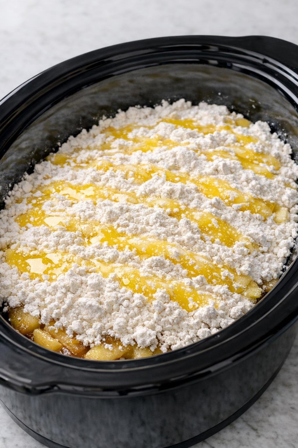 Droge cakemix en gesmolten boter laagje voor laagje in een slowcooker.