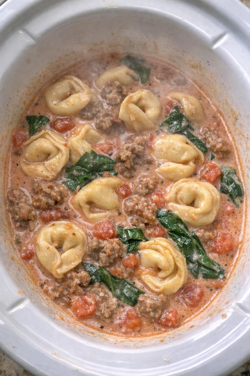 Close-up of a creamy sausage tortellini soup in a white slow cooker crock