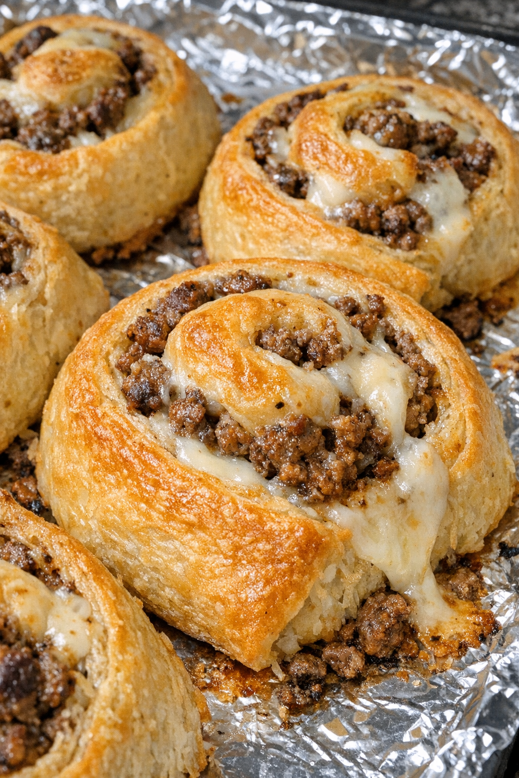 Oven baked beef crescent swirls on a foil-lined baking sheet